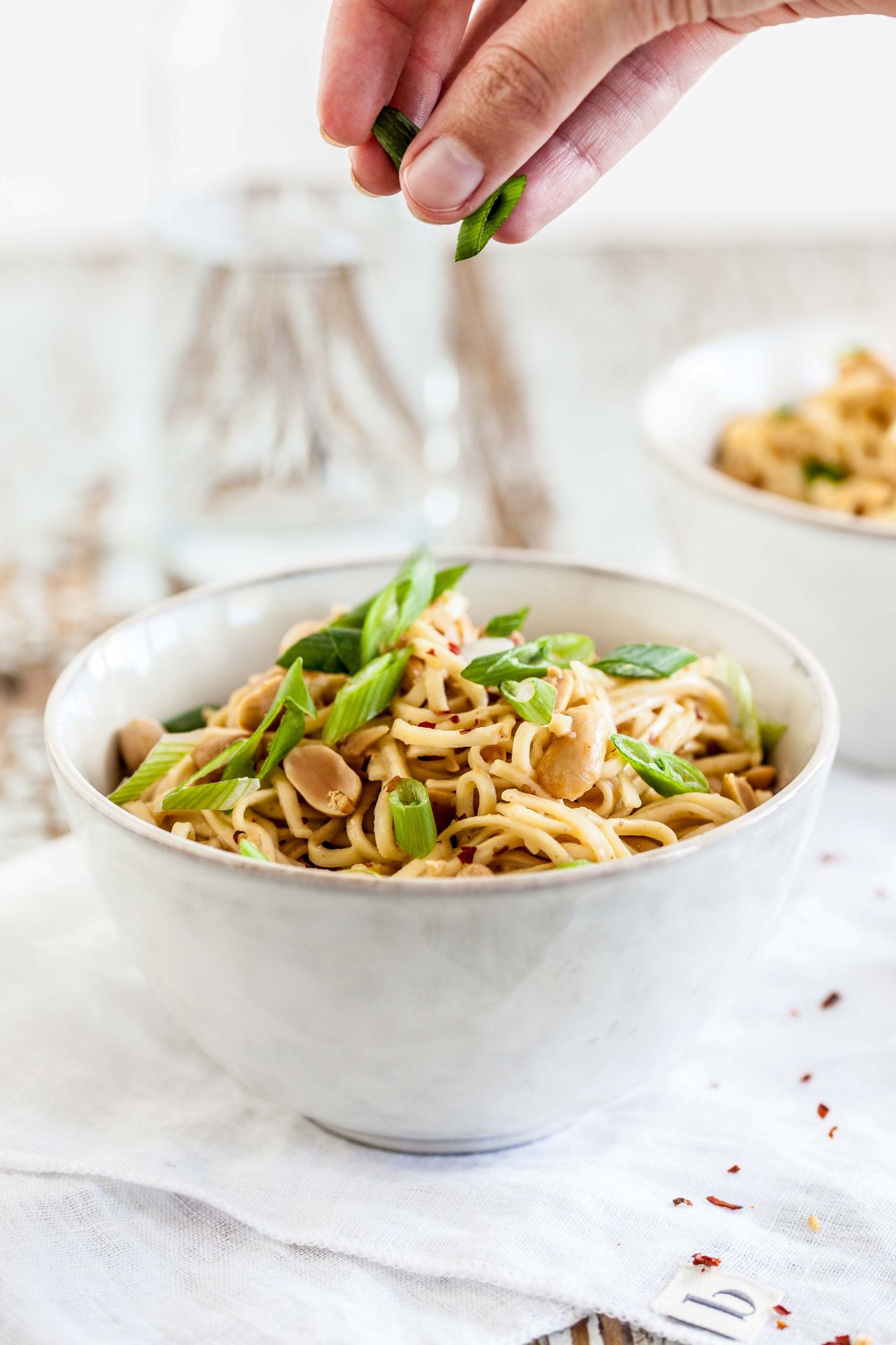 cropped-hand-woman-adding-chopped-scallions-noodles-bowl-table